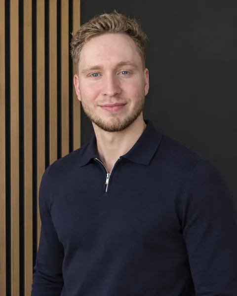 Paulius im dunkelblauen Pullover vor einer Holzlamellenwand